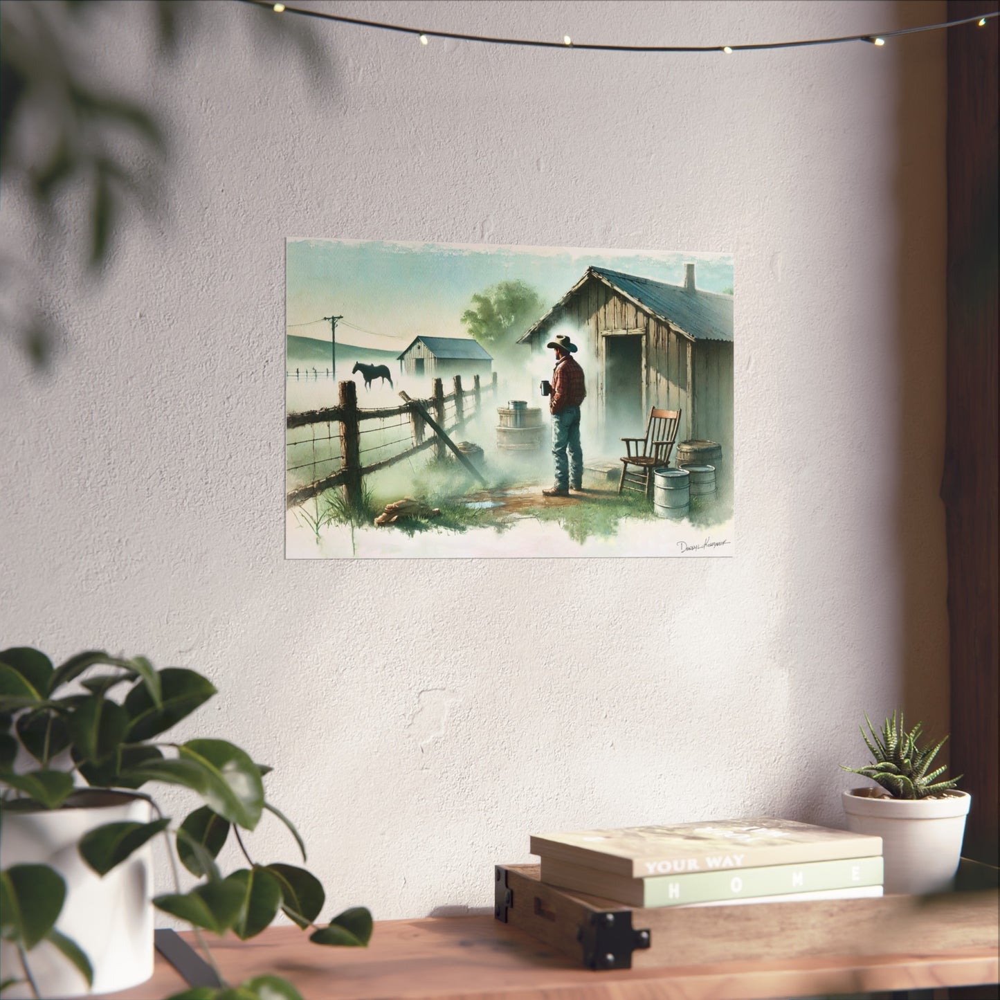 Poster of a cowboy by a cabin on a wall above a desk with plants.