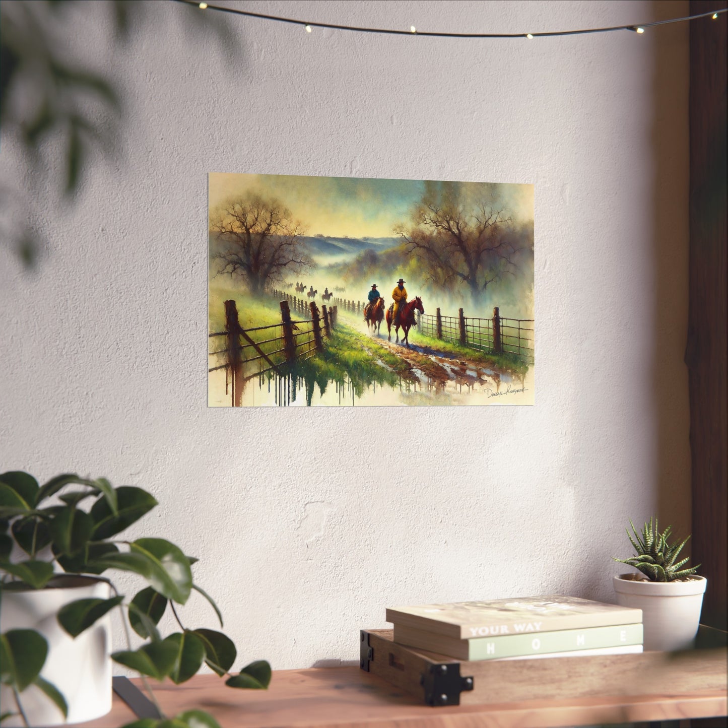 Painting of two cowboys on horseback by a fence on a wall above a desk with plants.