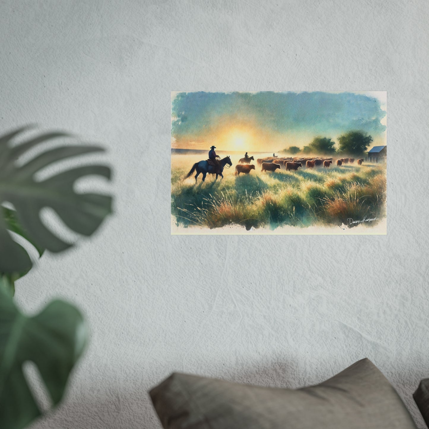 Art print of a sunset scene with cowboys on horseback and animals in a field, hanging on a wall.
