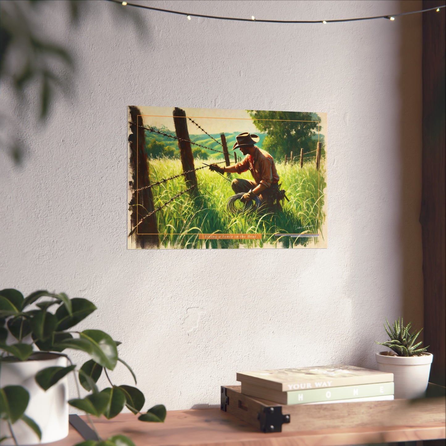 Poster of a cowboy working on a fence in a field hanging on a wall above a desk with plants.