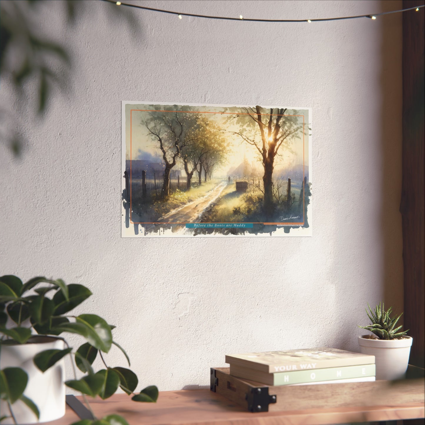 Fine art print of a scenic landscape on a wall above a desk with plants and books.