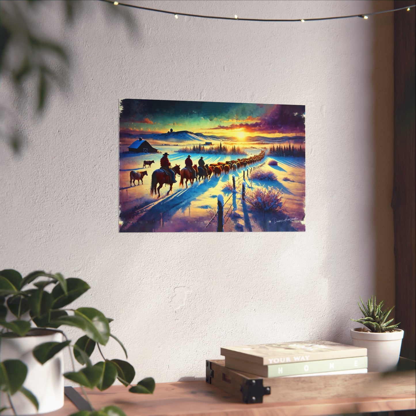 Wall art of a sunset scene with cowboys on horses and animals in a snowy landscape, hanging on a white wall.