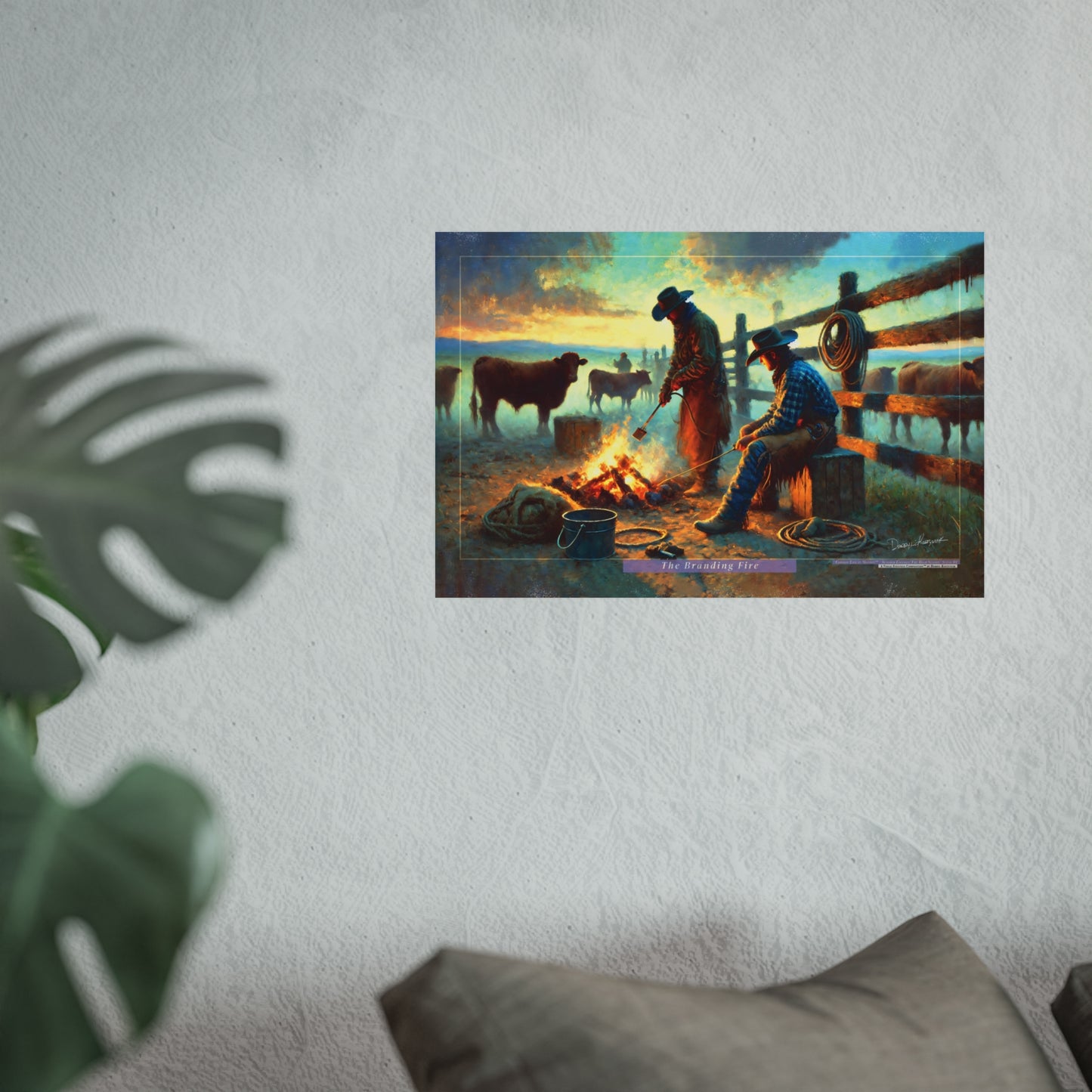 Poster of two cowboys around a branding campfire with cattle in the background, on a white wall.