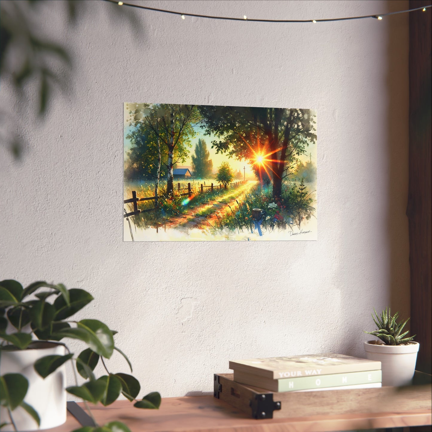Painting of a sunset over a forest path on a wall above a wooden desk with plants.
