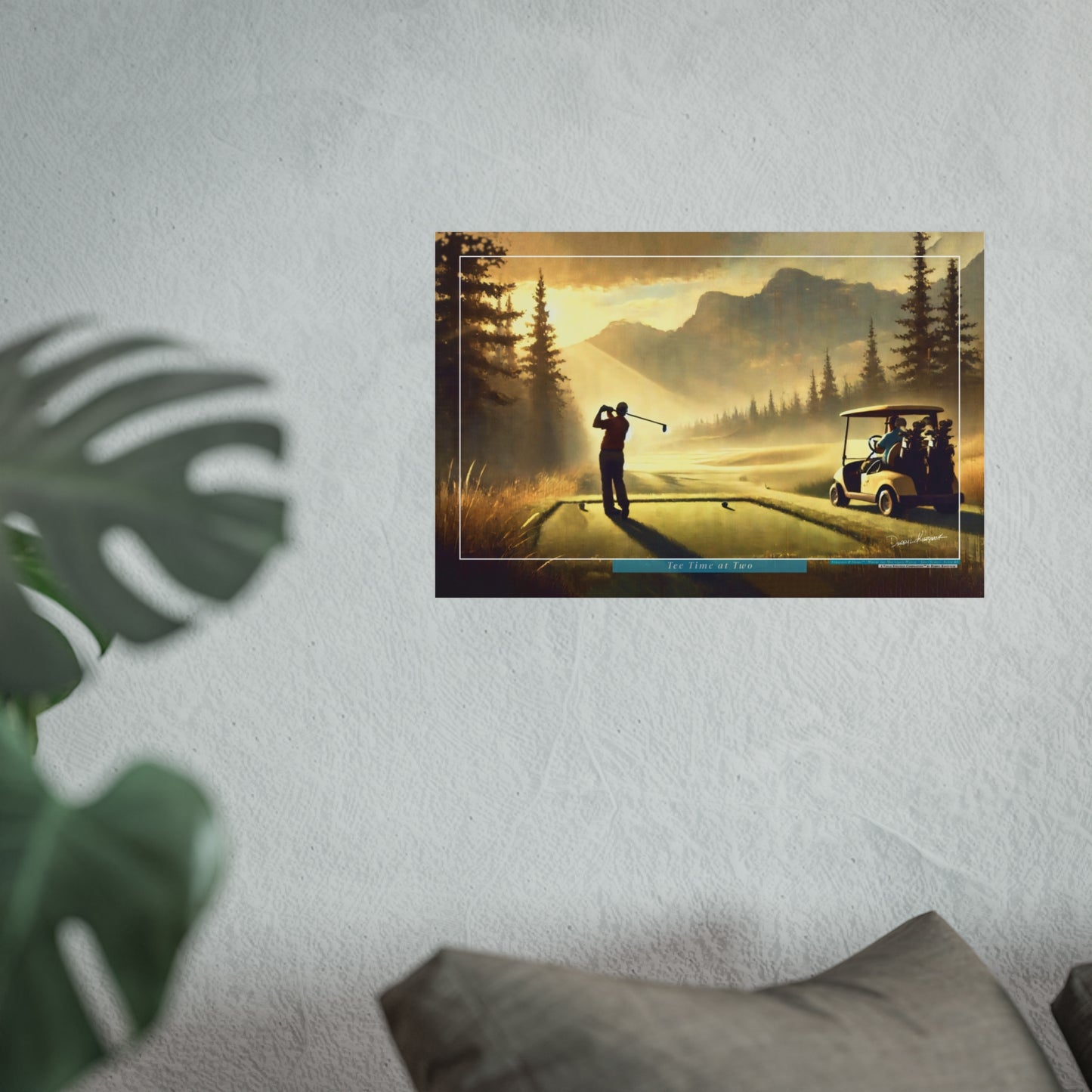 Framed artwork of a golf scene with a golfer and cart on a golf course with mountains in the background, displayed on a wall.
