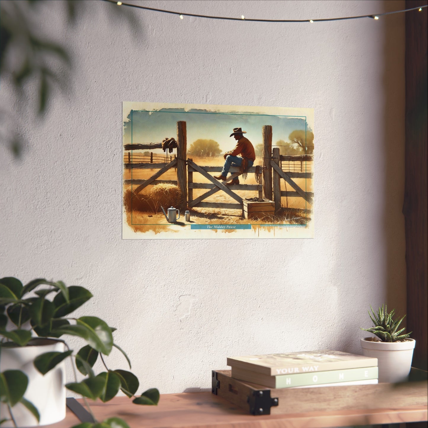 Poster of a cowboy on a wooden gate in a scenic landscape, displayed on a wall with plants and books below.