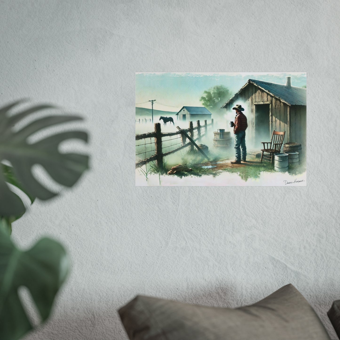 Poster of a cowboy by a fence with a horse on a wall, with a plant and pillow in the foreground.