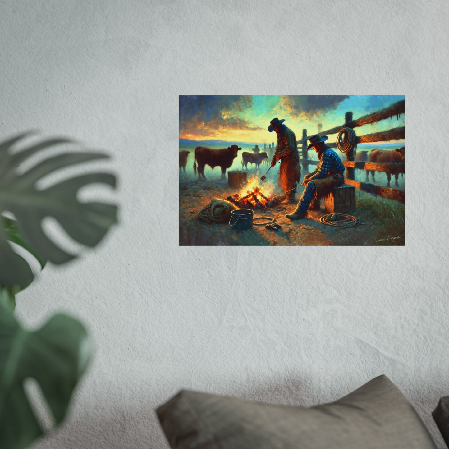 Art print of cowboys around a campfire with cattle on a wall, with a plant and pillow in the foreground.