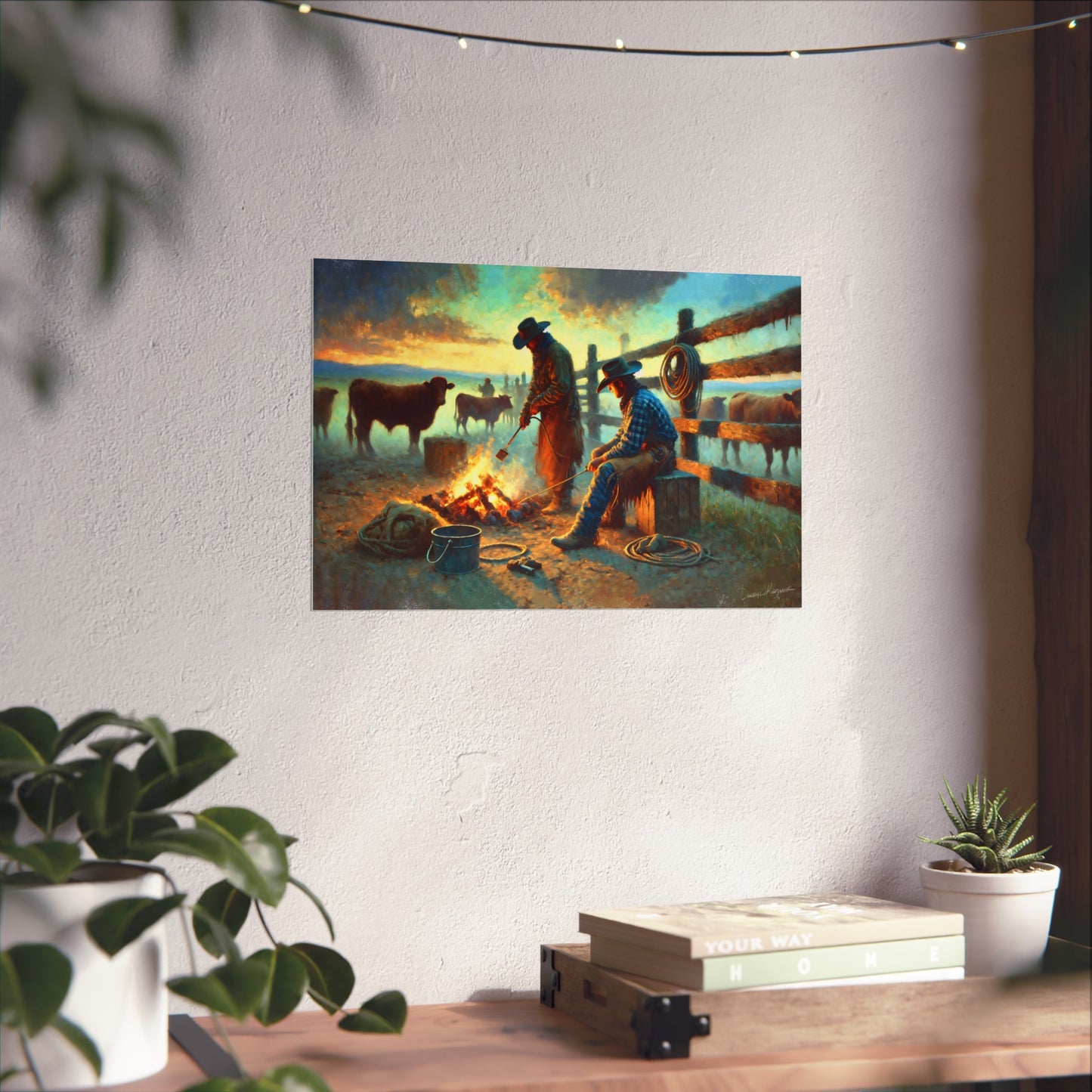 Painting of two cowboys by a campfire on a wall above a desk with plants.