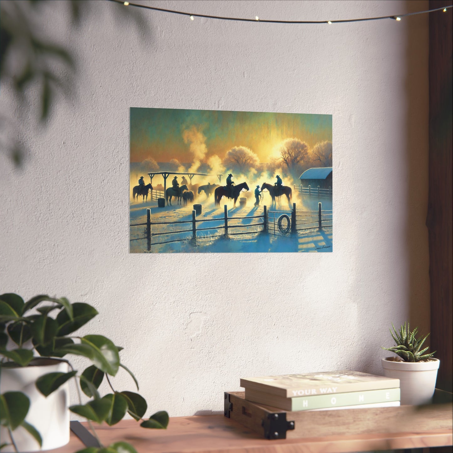 Silhouette of cowboys on horses at sunset with a wooden fence, framed on a wall above a desk.