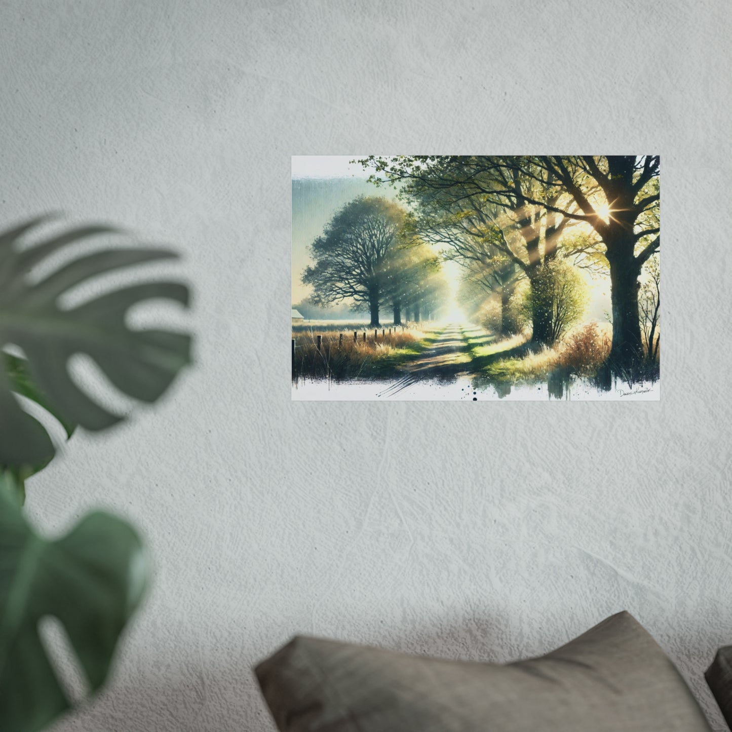 Framed artwork of a country road scene on a wall with a plant and pillow in the foreground.