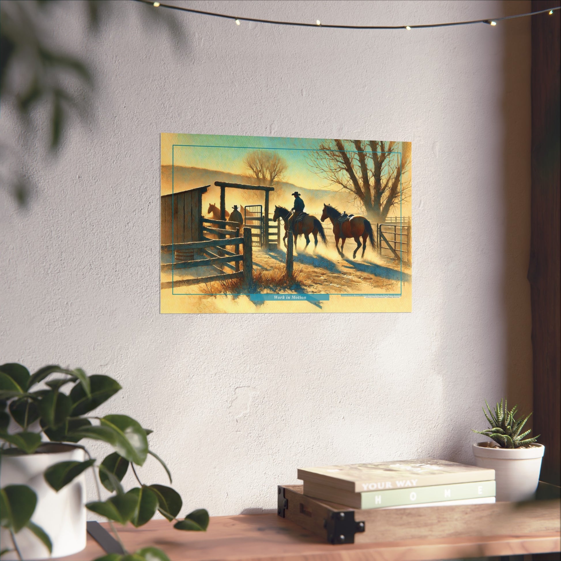 Poster of cowboys on horses at a fence on a wall above a desk with plants.