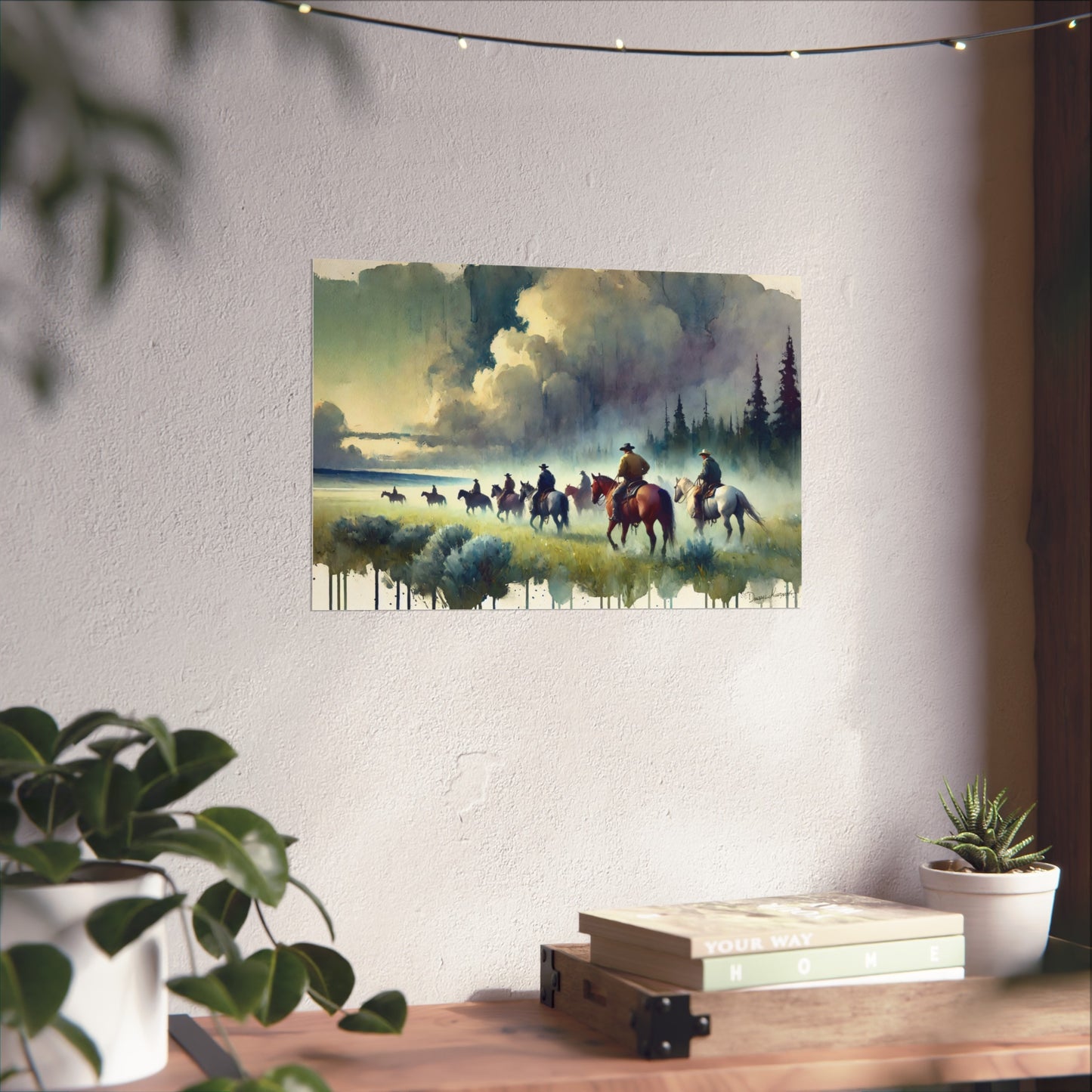Painting of cowboys on horses near a river on a wall above a desk with plants.