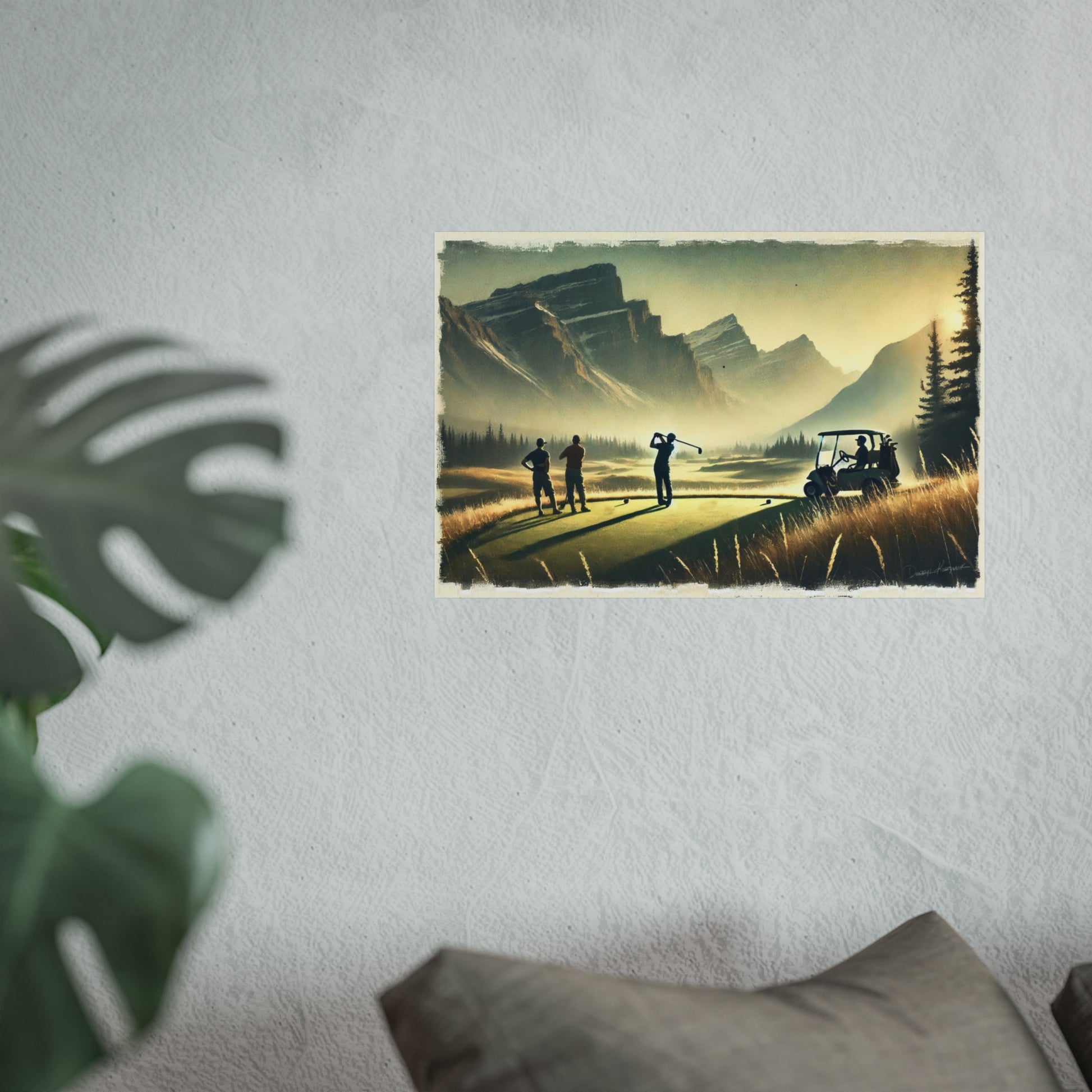 Poster of a mountainous golf scene on a wall with a plant and pillow in the foreground.