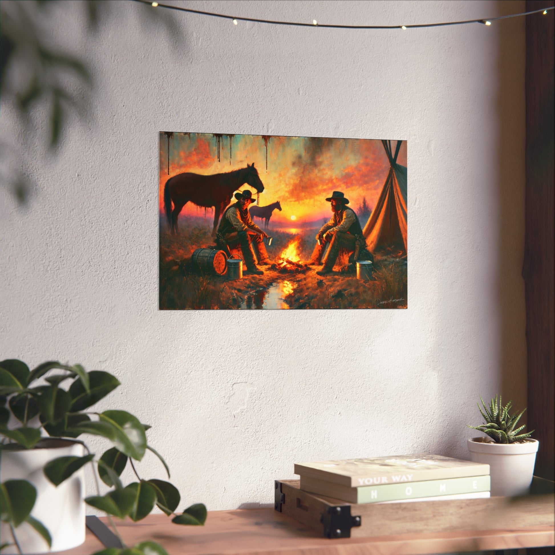 Canvas print of two cowboys by a campfire with horses on a white wall, below string lights.