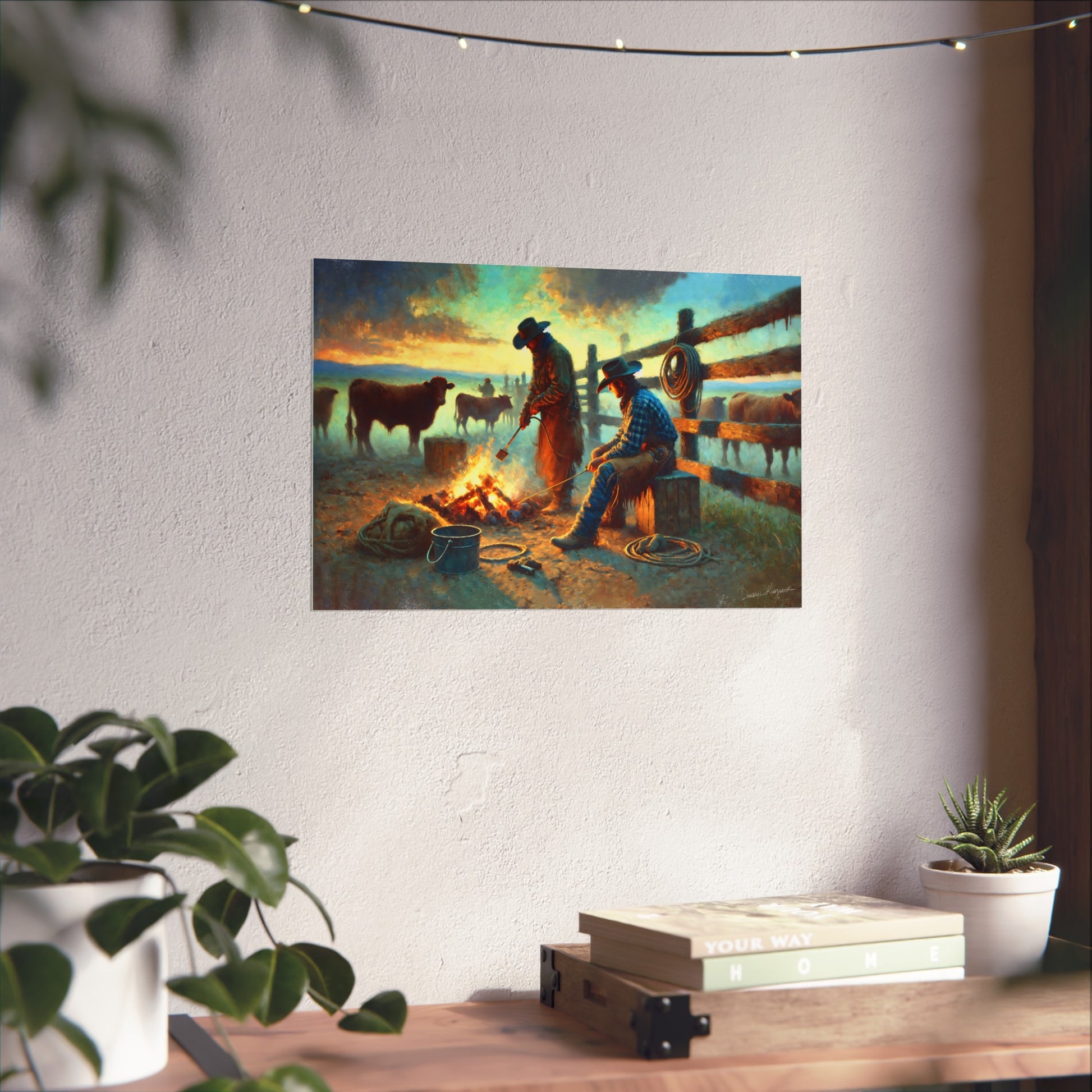 Painting of two cowboys by a campfire on a wall above a desk with plants.